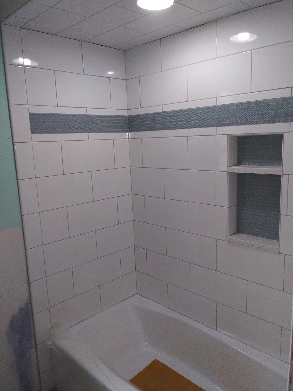 White subway tile shower with a charcoal herringbone accent band and built-in niches